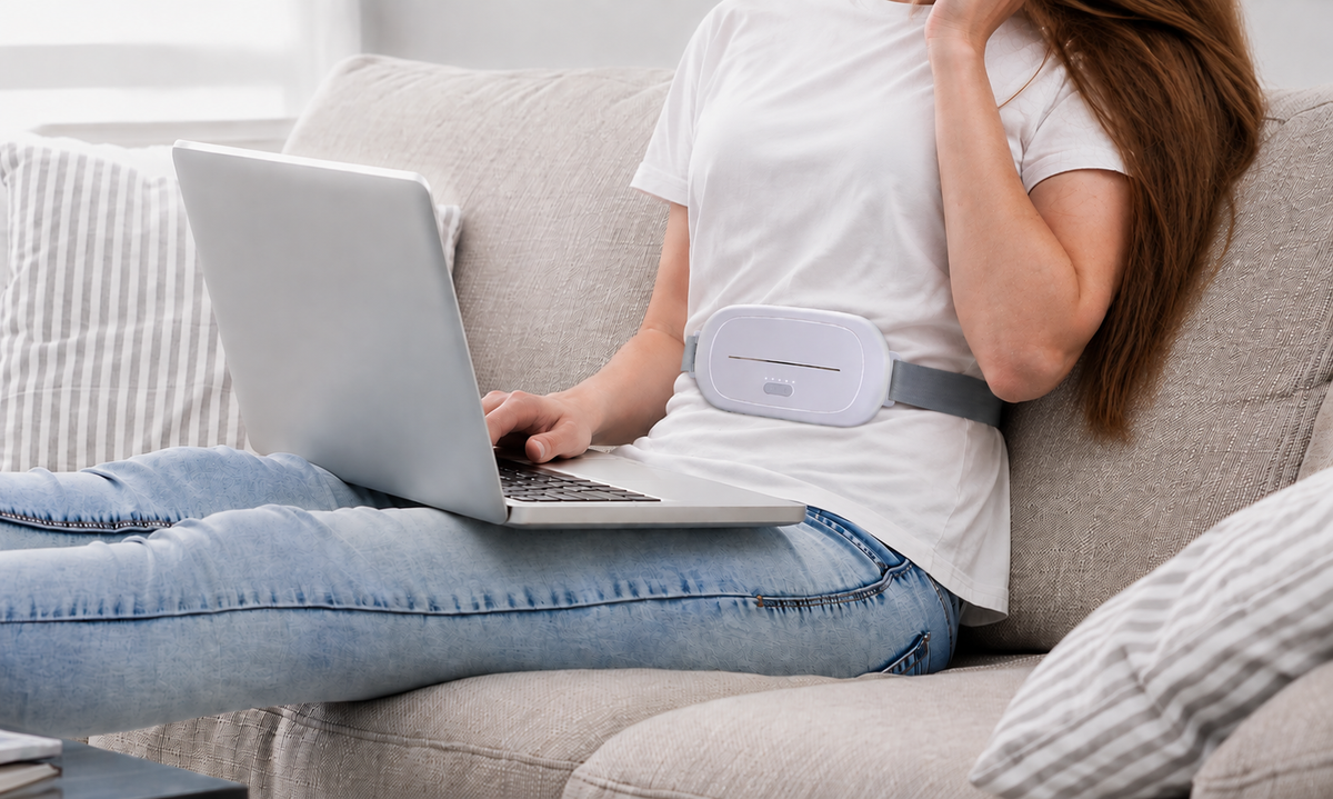 Woman working on a laptop on the sofa while wearing the Asheraa heat pad under her t-shirt